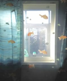 some goldfish are swimming in the water by a window with blue curtains and fish on it