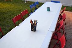 a long white table with red chairs and pencils in a cup on the top