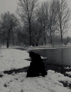 a person kneeling in the snow next to a river