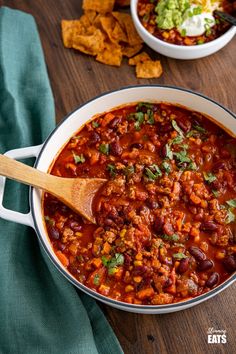 two bowls of chili with tortilla chips on the side and a wooden spoon