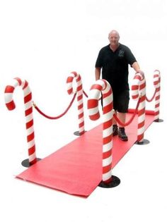 a man standing next to red and white candy canes on top of a red carpet