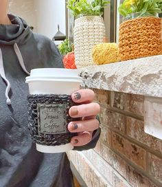 a woman holding a coffee cup in her right hand while standing next to a brick wall