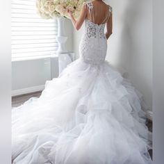 a woman in a white wedding dress holding a bunch of flowers and looking at the window