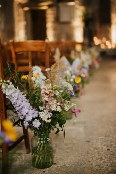 a row of wooden chairs sitting next to each other with vases filled with flowers