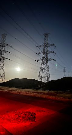 the sun is setting behind power lines and red light in the dark night sky,