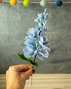 a hand holding a blue flower in front of a chalkboard with easter eggs hanging from it