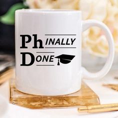 a white coffee mug with the words ph finally done on it and a graduation cap