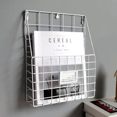 a white wire basket hanging on the side of a wall next to a book shelf