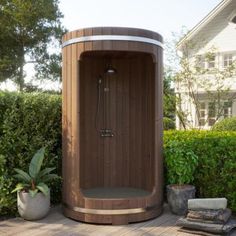 a large wooden sauna sitting on top of a wooden deck next to bushes and potted plants