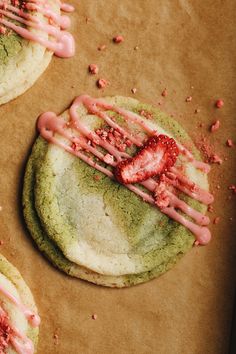 three cookies with pink icing and strawberries on top