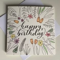 a card with the words happy birthday written in black ink on top of it, surrounded by flowers and leaves