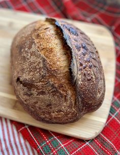 a loaf of bread sitting on top of a wooden cutting board next to a red and white checkered table cloth