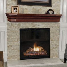 a fire place in a living room with a clock on the mantle and pictures above it