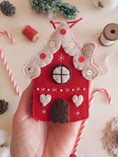 a hand holding a red felt house ornament with buttons and decorations around it