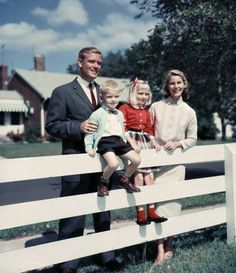 a man and two children are sitting on a white fence with their father standing next to them