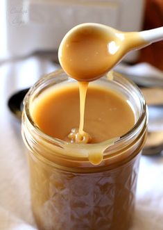 a spoon full of caramel sauce being poured into a jar