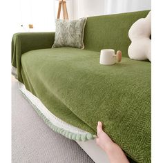 a green couch covered with a blanket and some coffee mugs on the table next to it