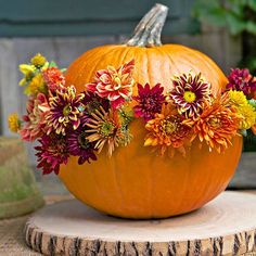 a pumpkin decorated with flowers sitting on top of a tree stump