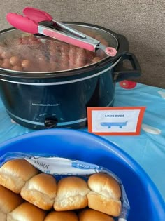 hot dogs and buns in the crock pot on a blue tablecloth with pink utensils