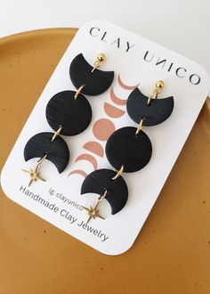 four black and gold earrings with stars on the bottom, sitting on top of a plate