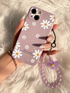 a hand holding a phone case with daisies on it and a beaded keychain