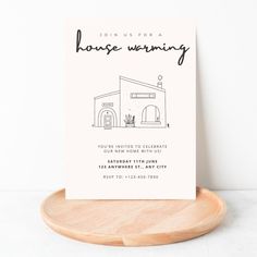 a card with the words house warming on it sitting on a wooden plate next to a white wall