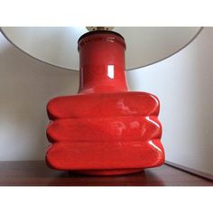 a red vase sitting on top of a wooden table next to a wall mounted mirror