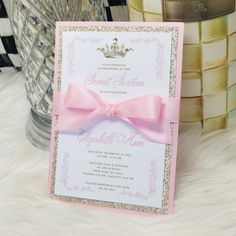 a pink and gold wedding card with a princess crown on the front, sitting on a white furnishing