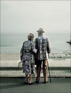 an older couple standing next to each other near the ocean with a quote above them