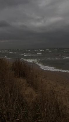 an empty beach with waves coming in to the shore and dark clouds overhead over the water