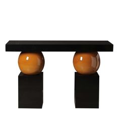 an orange vase sitting on top of a black table next to two smaller brown balls