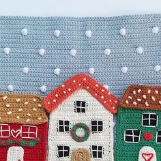 a crocheted christmas scene with houses and wreaths on the front, along with snowflakes in the background