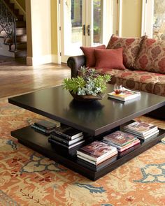 a living room with couches, coffee table and books on the floor in front of it