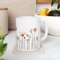 a white coffee mug sitting on top of a counter next to a bowl of fruit