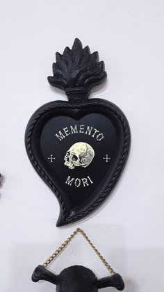 a black heart shaped clock with a skull hanging from it's side and the words mementoo mori written on it