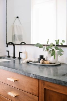 a bathroom counter with soap, toothbrushes and a plant on it in front of a mirror