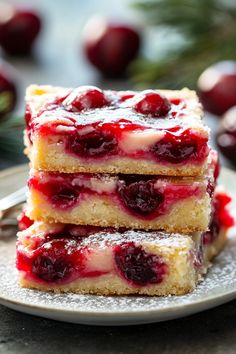 three pieces of cherry cheesecake on a plate with powdered sugar and fresh cherries in the background