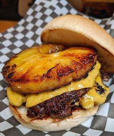 a burger with meat, cheese and pineapple is on a checkered tablecloth