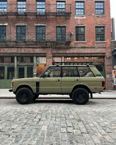 an suv parked in front of a brick building on a cobblestone street next to tall buildings