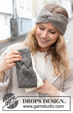 a woman wearing a headband and holding up a pair of gray knitted mitts