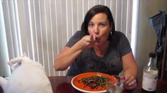 a woman sitting at a table with a plate of food in front of her mouth