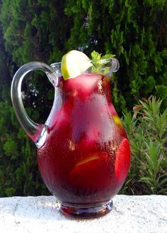 a pitcher filled with red liquid sitting on top of a table next to some trees