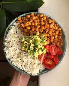 a plate with rice, tomatoes and chickpeas on it next to a hand