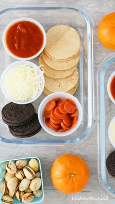 two plastic containers filled with food on top of a counter next to oranges and crackers