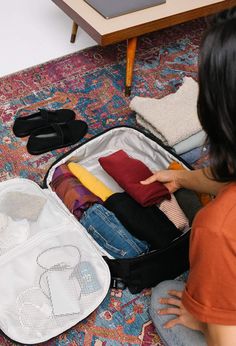 a woman sitting on the floor next to an open suit case filled with clothing and shoes