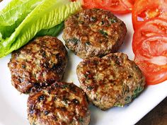 four hamburger patties on a plate with lettuce and tomatoes next to them