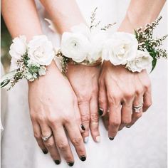 two brides holding hands with white flowers on their wristlets and wedding rings in each hand