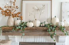 white pumpkins and greenery sit on a mantel in front of a fireplace