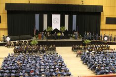 graduates in blue caps and gowns are seated on the stage