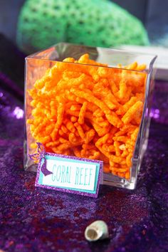 some kind of food in a glass container on a table with purple sequins